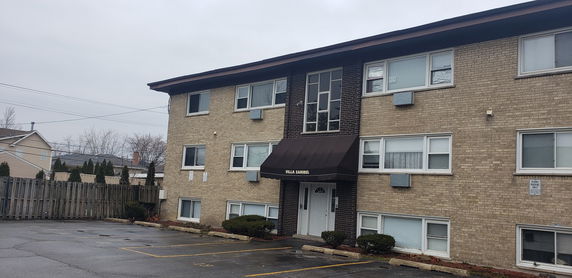 Front view of a three-story apartment building with a canopy entrance and multiple windows.