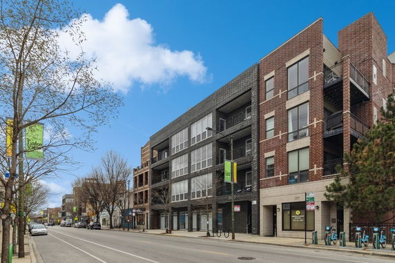 Front view of a modern multi-story building with a brick facade and large windows.
