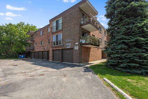 Front view of a brick apartment building with balconies and garages on the ground level.