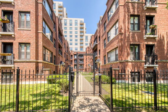 Front view of two adjacent multi-story brick apartment buildings with a gated entry and a pathway leading inside.