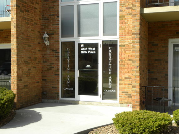 Entrance view of a brick building with glass doors displaying the name 'Crestline Arms Condos'.