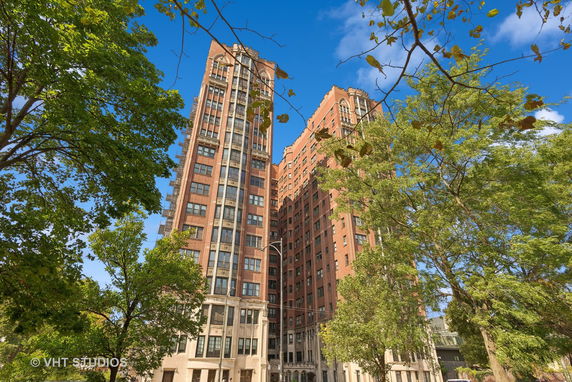 View of a tall residential building with a classic facade, surrounded by trees.