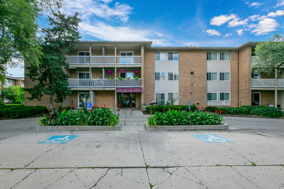 Front view of a three-story apartment building with balconies and accessible parking spaces.