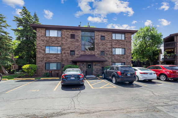 Front view of a three-story brick apartment building with a parking area in front.