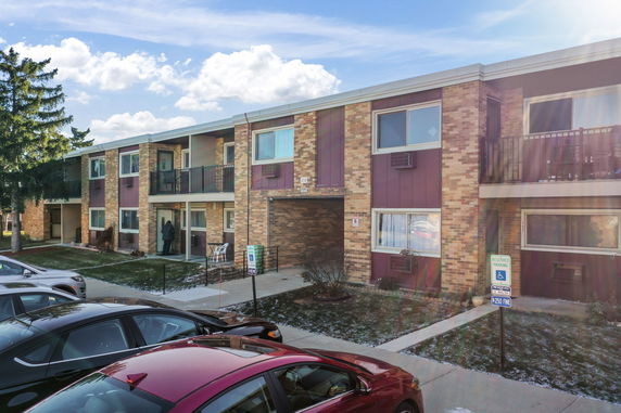 Front view of a two-story apartment building with brick facade and a mix of large and small windows.