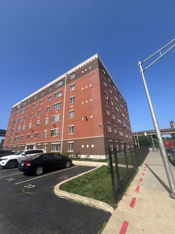 Front view of a multi-story brick apartment building with parking area.