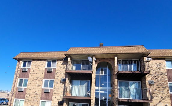 Front view of a multi-story apartment building with balconies and a satellite dish.