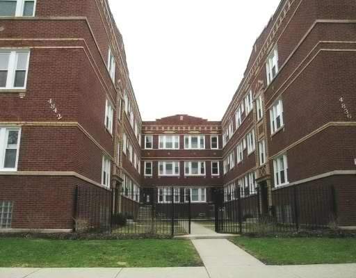 Front view of a multi-story brick apartment building with gated entrance.