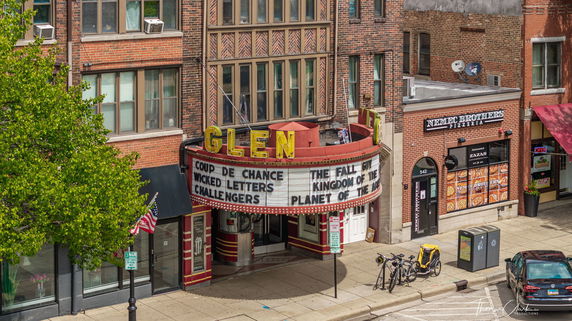 View of a brick building with a vintage theater marquee and adjacent storefronts.
