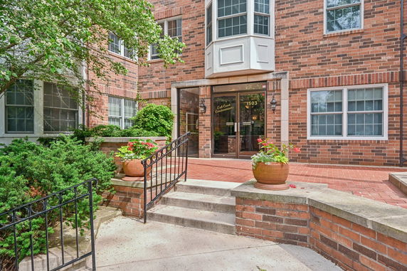Front view of a brick condominium entrance with glass doors and planters.