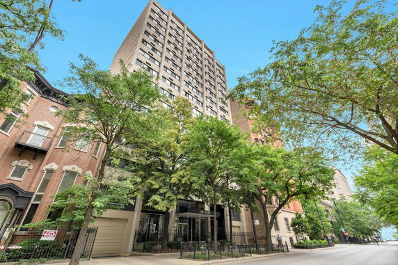 Front view of a multi-story residential building with trees along the sidewalk.