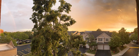 Panoramic view of a residential area with houses, trees, and a parking lot at sunset.