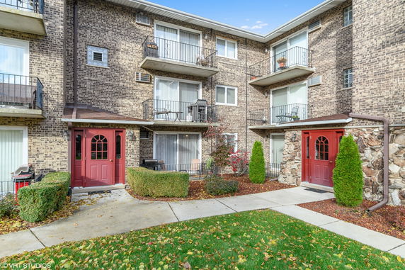 Front view of a multi-story residential building with balconies and red entrance doors.