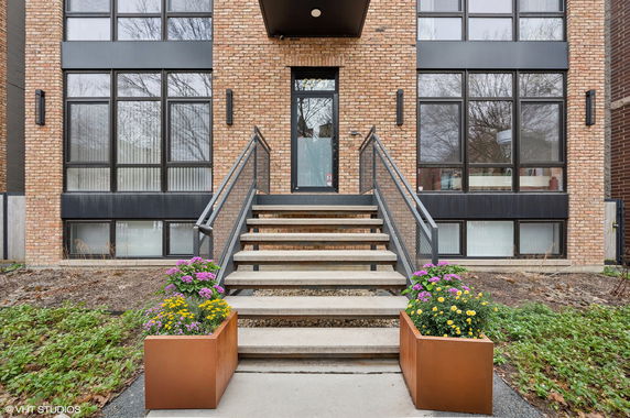 Front view of a modern brick building with large windows and a staircase leading to the entrance.
