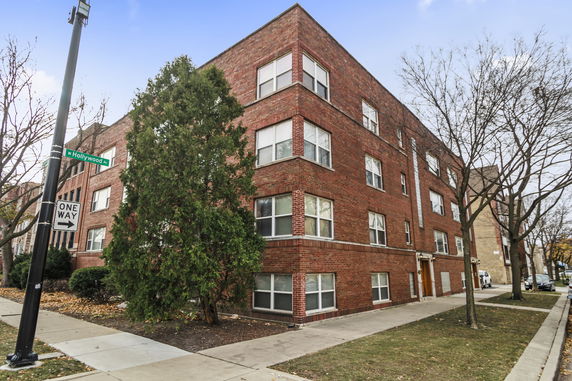 Front view of a brick multi-story building on a street corner.