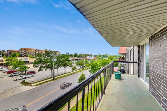 Balcony view overlooking a street with a parking area and commercial buildings in the background.