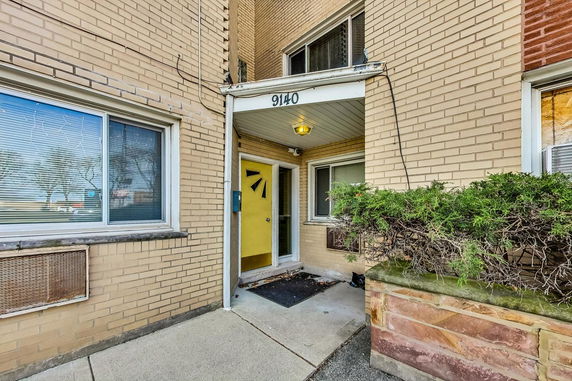 Front view of a brick building with a yellow door and address number.