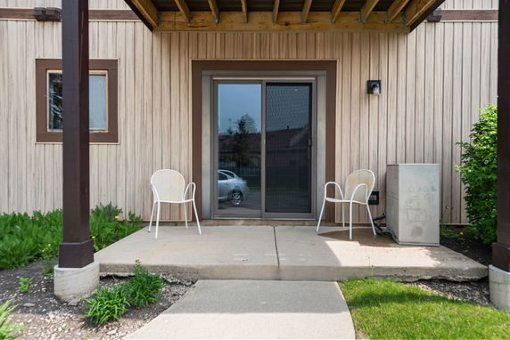 Front view of a building with sliding glass door and two chairs on a concrete slab.