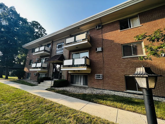 Front view of a three-story building with balconies and brick facade.