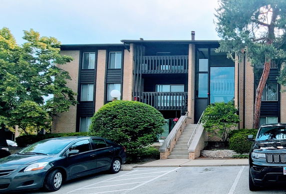 Front view of a three-story apartment building with a staircase leading to the entrance.