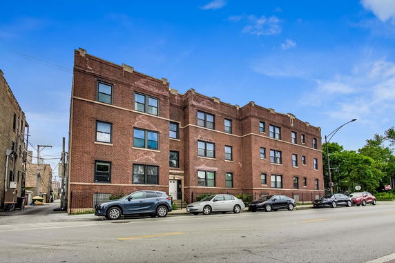 Front view of a three-story brick building with multiple windows and a sidewalk in front.
