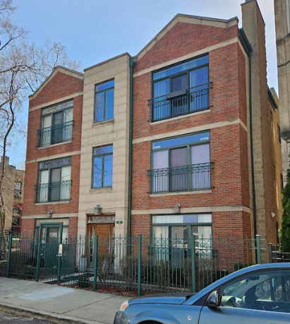 Front view of a three-story brick apartment building with balconies and a gated entrance.