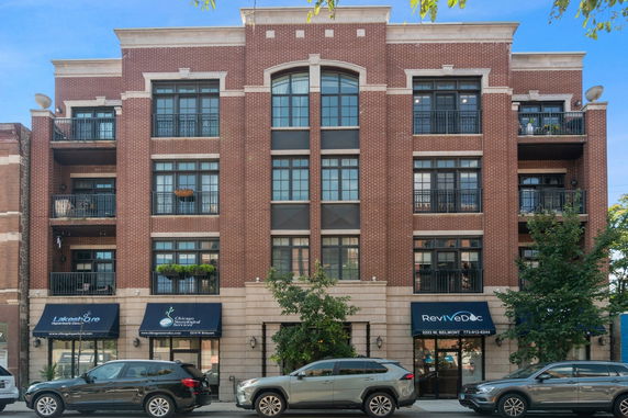 Front view of a multi-story brick building with balconies and commercial spaces on the ground floor.