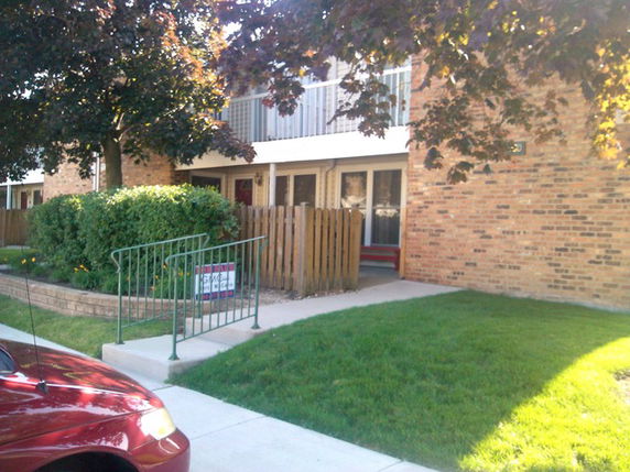 Front view of a brick apartment building with a small fenced patio and concrete walkway.