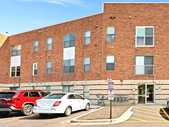 Front view of a three-story brick building with multiple windows and parked cars.