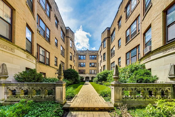Front view of a multi-story brick apartment building with landscaped walkway.