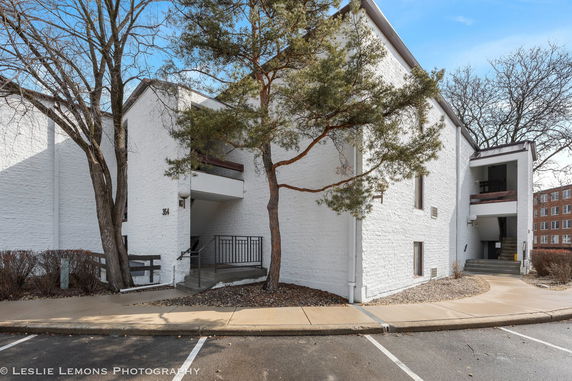 Front view of a white brick building with trees around and an entrance with steps.