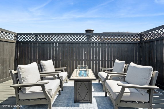 Rooftop with seating area featuring cushioned chairs arranged around a modern fire pit table.