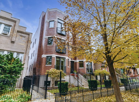 Front view of a multi-story brick building with wrought iron fence and stairs leading to the entrance.