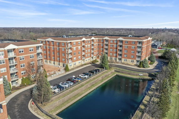 Front view of a multi-story brick apartment building with a parking area and a pond.