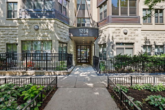 Front view of a multi-story building entrance with numbered canopy and surrounding garden.