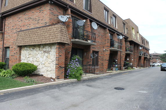 Front view of a multi-story brick apartment building with balconies and satellite dishes.
