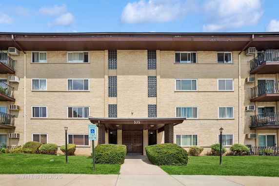 Front view of a multi-story apartment building with a central entrance and balconies.