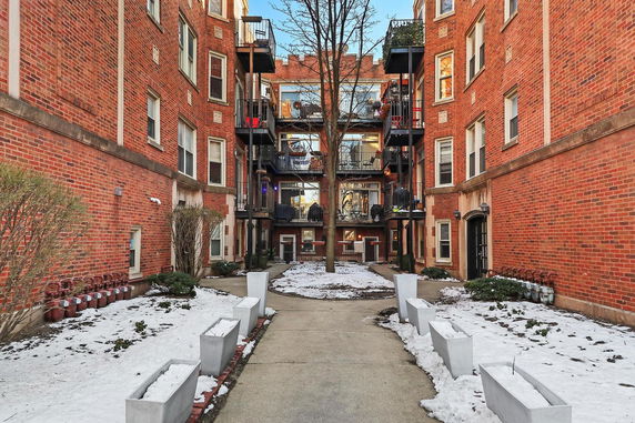Front view of a brick apartment building with balconies and a central pathway.