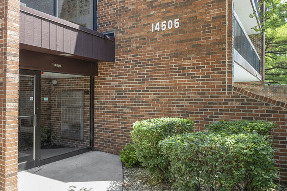 Front view of a brick building entrance with glass doors and shrubs.