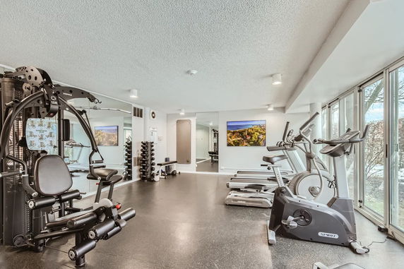 Indoor gym area with exercise equipment, mirrors, and large windows.