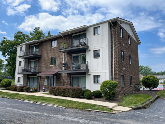 Front view of a three-story apartment building with balconies and brick exterior.