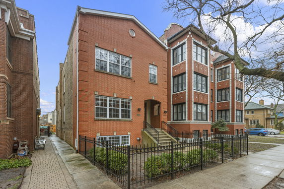 Front view of a multi-story brick building with large windows and a fenced entrance.