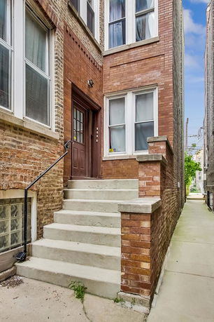 Front view of a brick building entrance with stairs leading to a wooden door.