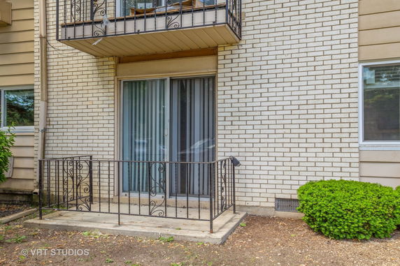 Brick exterior of a building with a small concrete patio and metal railing.