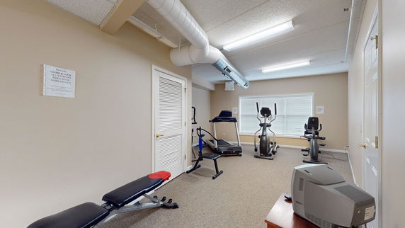 Room with exercise equipment including a treadmill and stationary bikes.