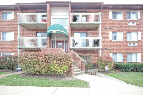 Front view of a multi-story brick apartment building with balconies and a central entrance.