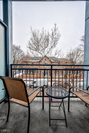 View from a balcony with chairs and a table overlooking a street and building.