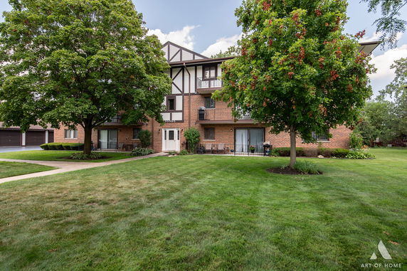 Front view of a multi-story brick building with balconies and large trees in the foreground.
