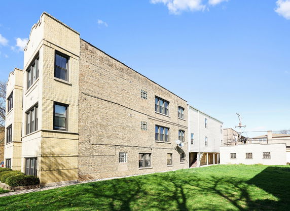 Side view of a multi-story brick building with multiple windows and a grassy area in front.
