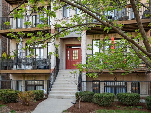 Front view of a multi-story building with balconies and a central red door entrance.